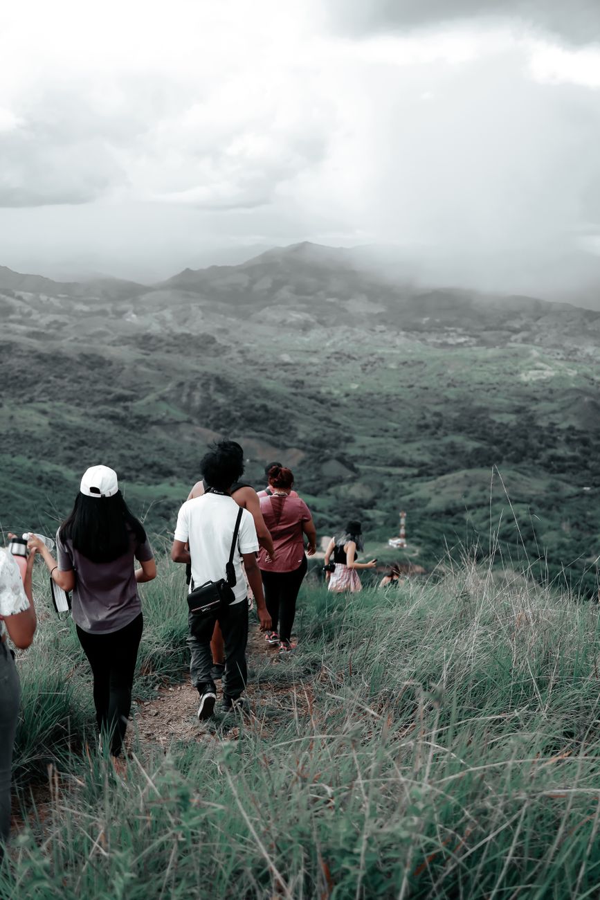 Group of hikers descending a mountain trail with a scenic view of a cloudy landscape.