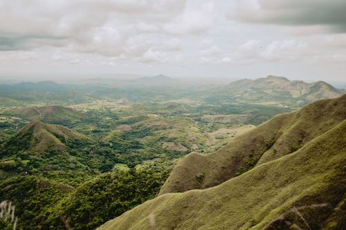 Free A scenic aerial view of a vast green mountain range under a cloudy sky. Stock Photo