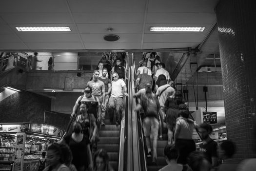 Monochrome photo of a busy escalator with people in motion at an indoor transit station.