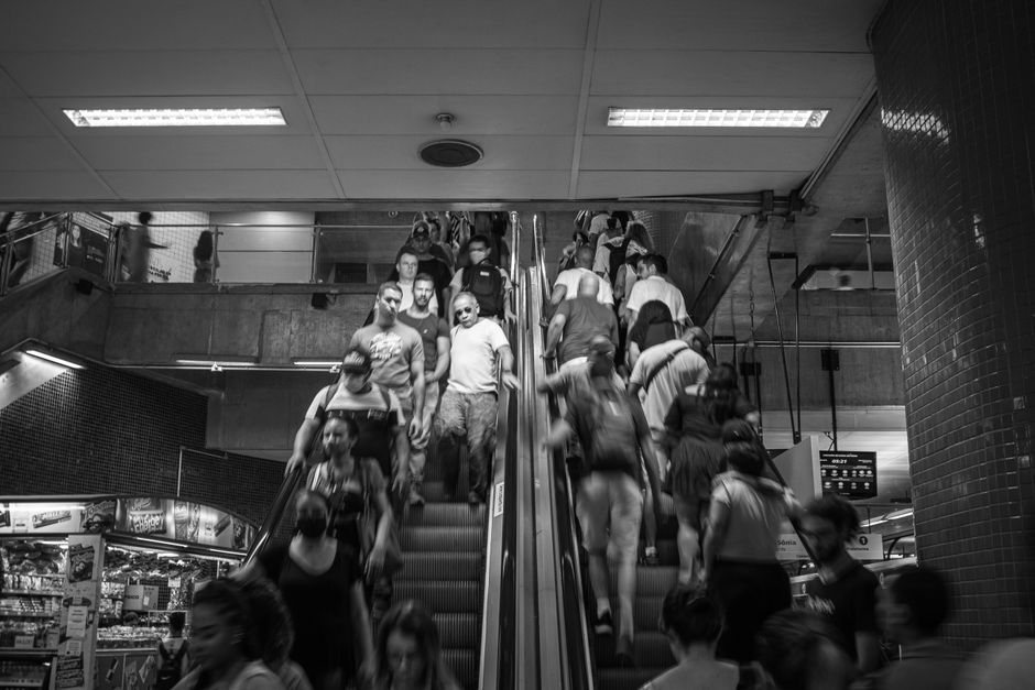 Foto en blanco y negro de una escalera mecánica concurrida con personas en movimiento en una estación de tránsito interior.