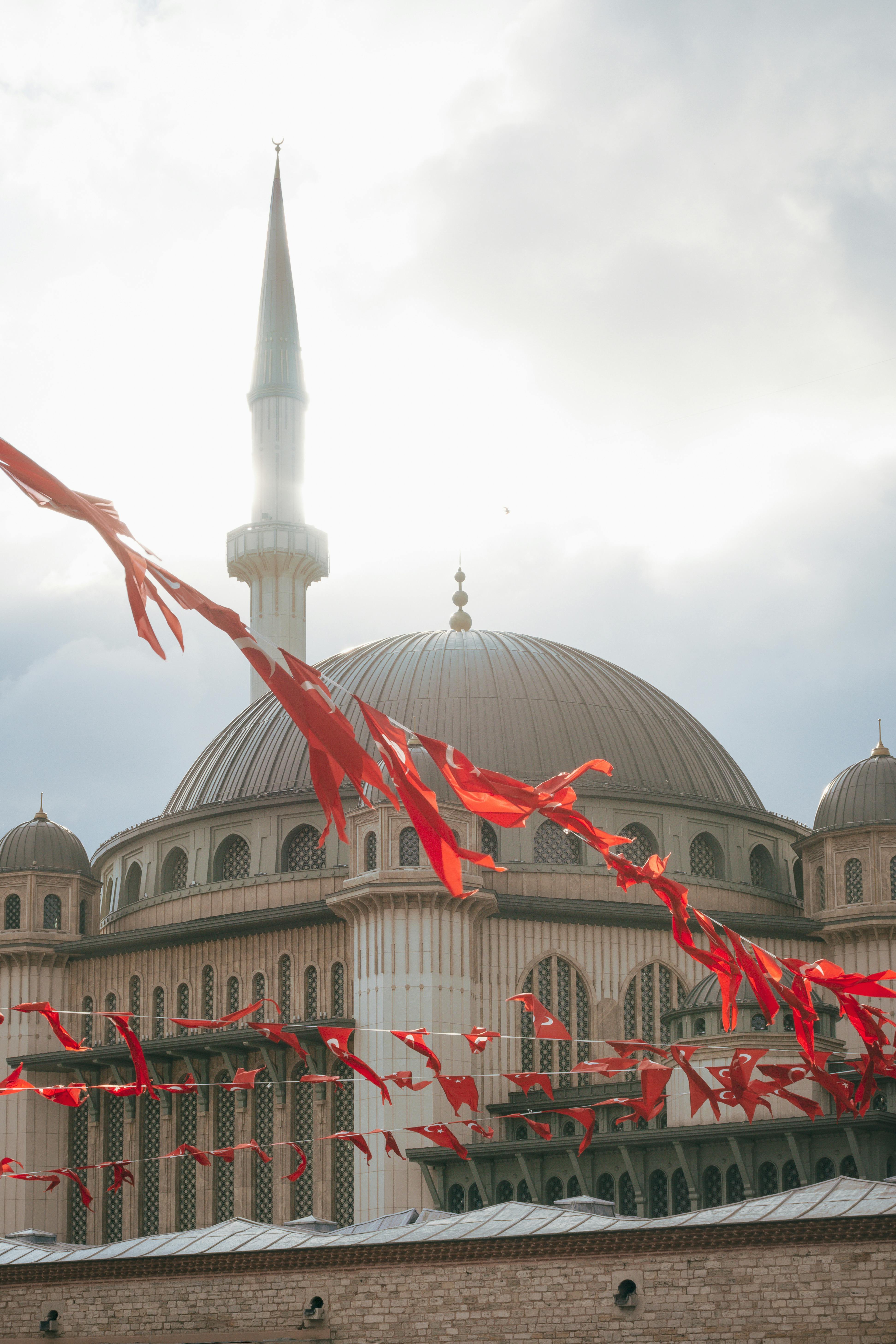 A mosque's dome and minaret with Turkish flags fluttering in the sunlight, Istanbul, Turkey.