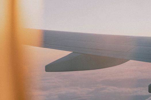 Capture of airplane wing flying above clouds at sunset, viewed from a window.