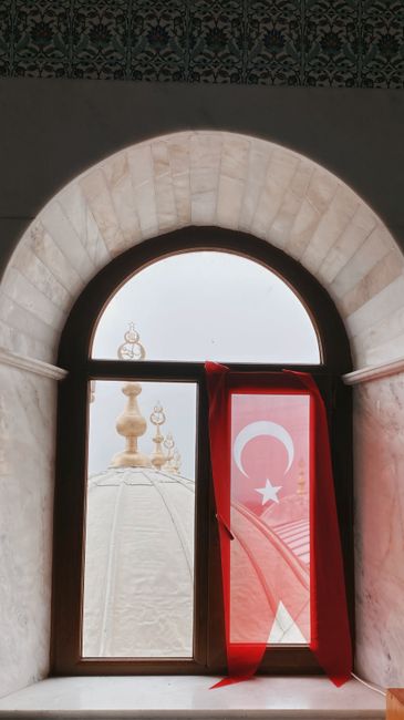 Turkish flag draped over a window with a mosque dome in the background.