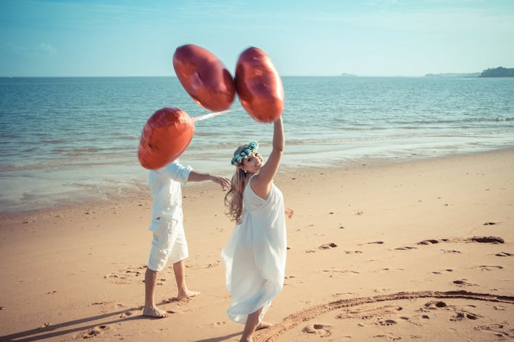 Young Couple Walking On A Beach With Red Balloons 