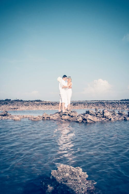 Bride and Groom Hugging on Rocks on Seashore