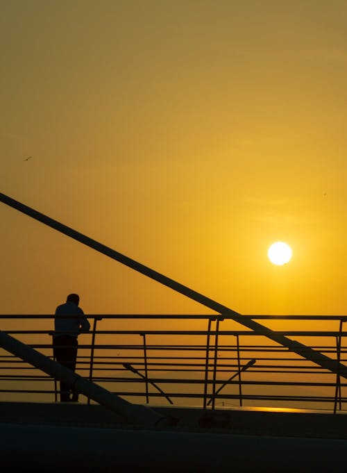 Silhouette of Man Standing on Bridge on Sunset