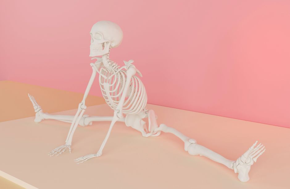 A white skeleton model practicing yoga in a pastel pink room.