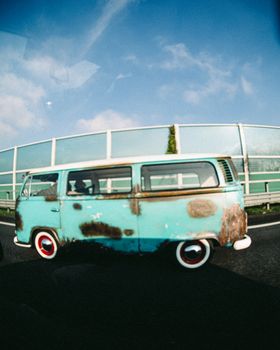 Old rusty campervan driving on a highway with a clear blue sky backdrop.
