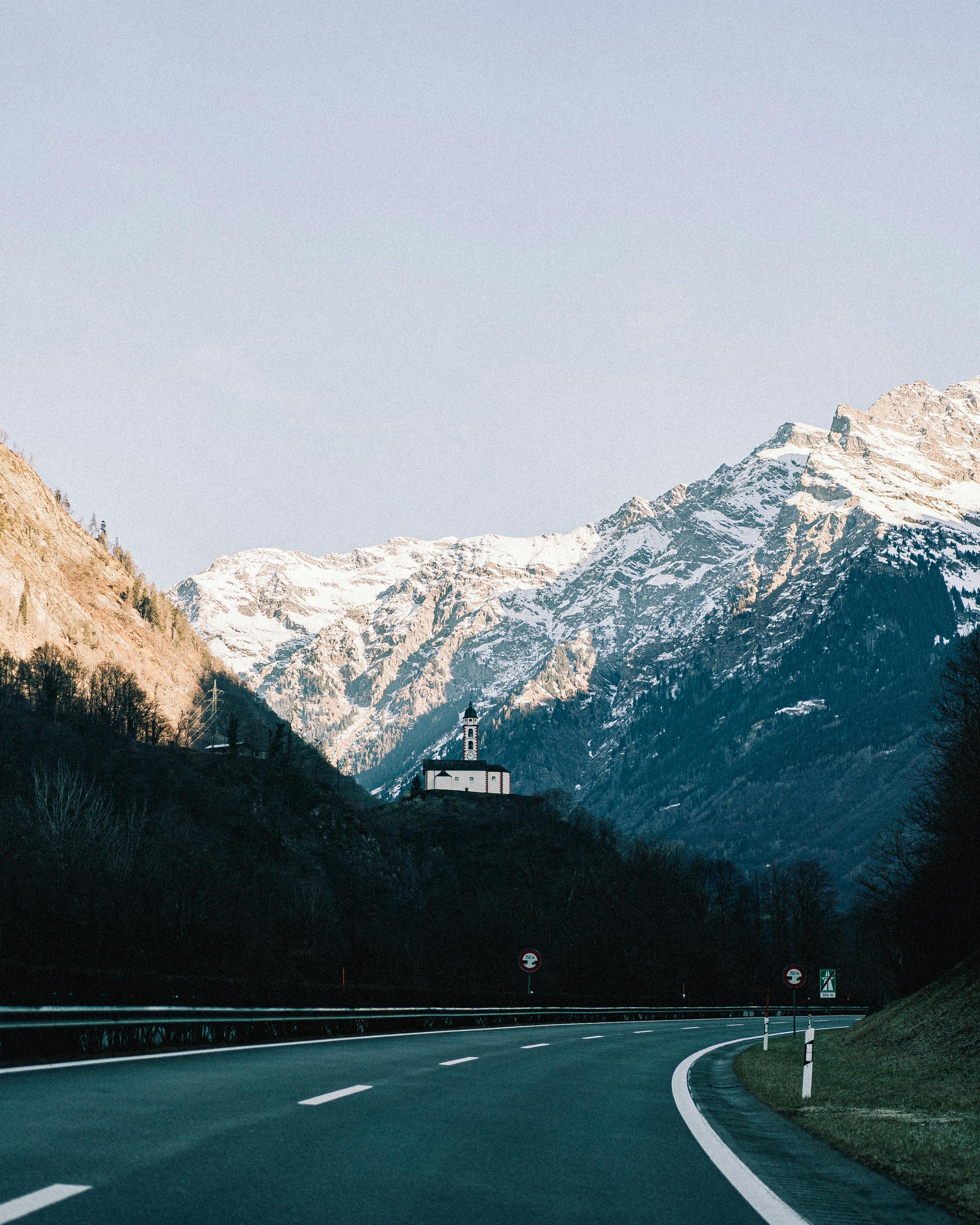 Beautiful winding road leading through the mountains with snow-capped peaks and clear blue skies.