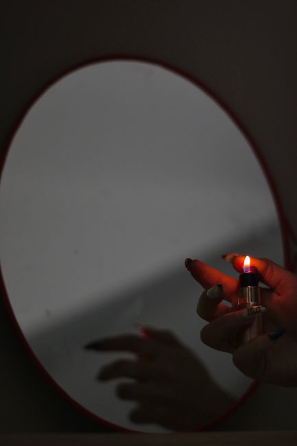 Artistic photo of a hand lighting a flame in front of a mirror, evoking introspection.