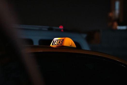 Close-up of an illuminated taxi sign reading 'Taksi' at night, providing a warm glow in the darkness.