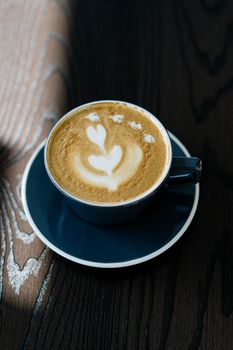 Top view of a coffee cup with latte art on a wooden table, showcasing intricate foam design.