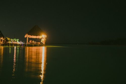 Free Serene tropical night view featuring illuminated gazebo over calm waters. Stock Photo