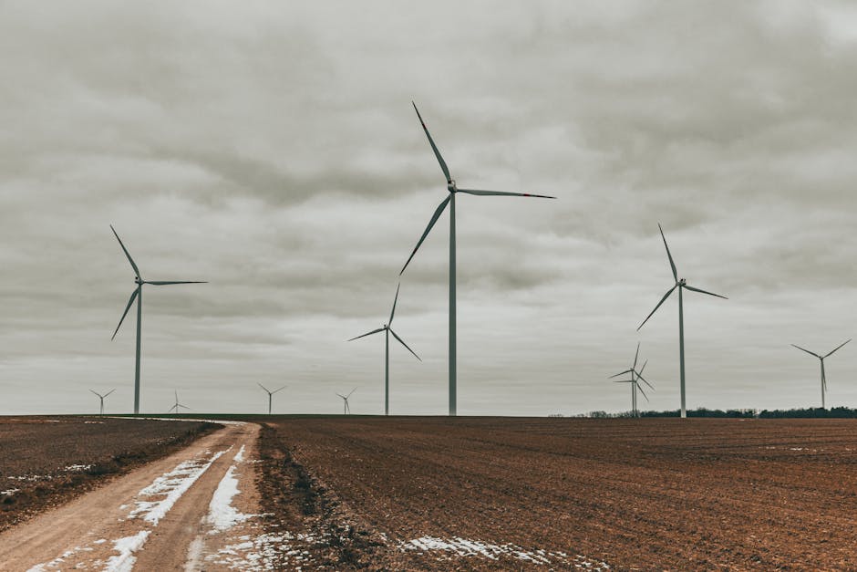 Wind turbines stand tall in an open, snow-dusted field under a cloudy sky, showcasing renewable energy.