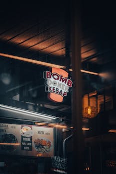 Moody street view of Bomb Doner Kebab illuminated sign and ceiling decor in urban nightlife setting.
