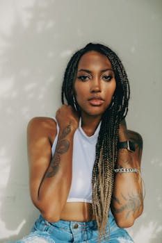 Fashionable woman with dreadlocks and tattoos posing confidently in casual clothes.