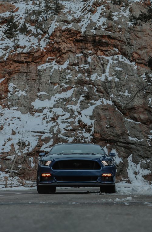 Free A blue car on a snowy road against a rocky hill in winter, showcasing travel and adventure vibes. Stock Photo