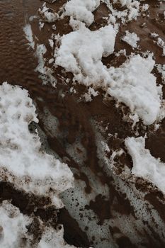 Close-up of snow-covered ground revealing underlying mud and frozen patterns.