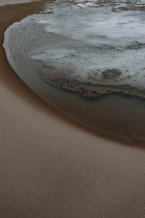 Free Aerial view of abstract patterns on a sandy beach with water and ice formations. Stock Photo