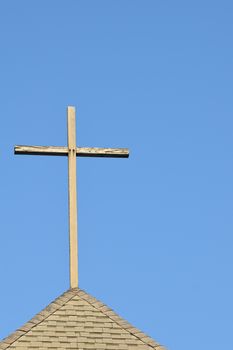 A weathered wooden cross stands on a church rooftop under a clear blue sky, symbolizing faith and spirituality.