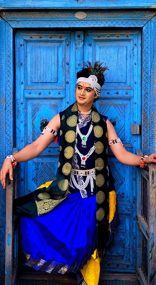 Free South Asian adult in vibrant traditional attire poses in front of a decorative blue door in Nandgaon, India. Stock Photo