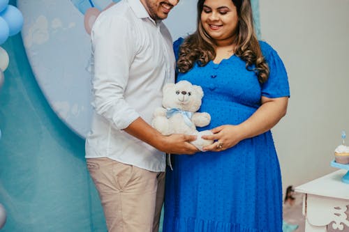 Smiling Woman in Blue Dress and Man in Shirt Standing and Holding Teddy Bear