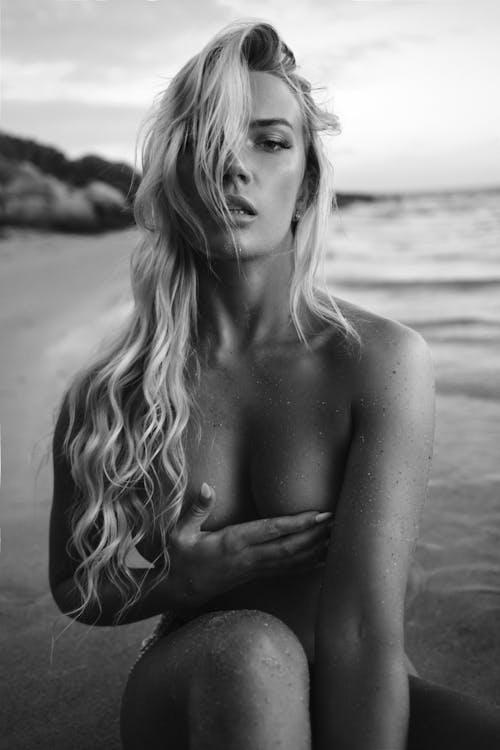 Black and White Photo of Topless Woman Sitting on Beach