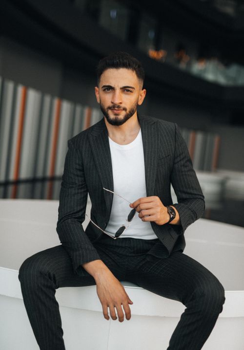 Free Elegant man in suit posing indoors with sunglasses, exuding contemporary style. Stock Photo