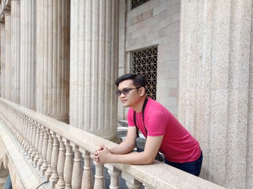 Free Man wearing sunglasses and pink t-shirt leaning on railing with stone columns in the background. Stock Photo
