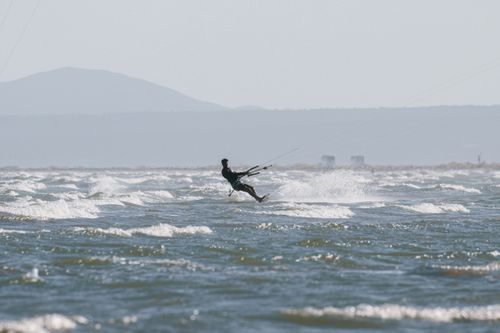 Free Silhouette of a kiteboarder gliding over waves in a sunny seascape. Stock Photo