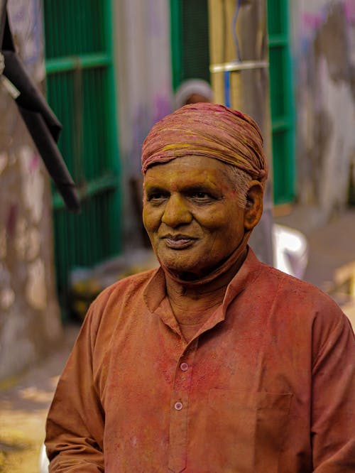 Elderly Man in Traditional Clothes Covered in Colorful Powder 