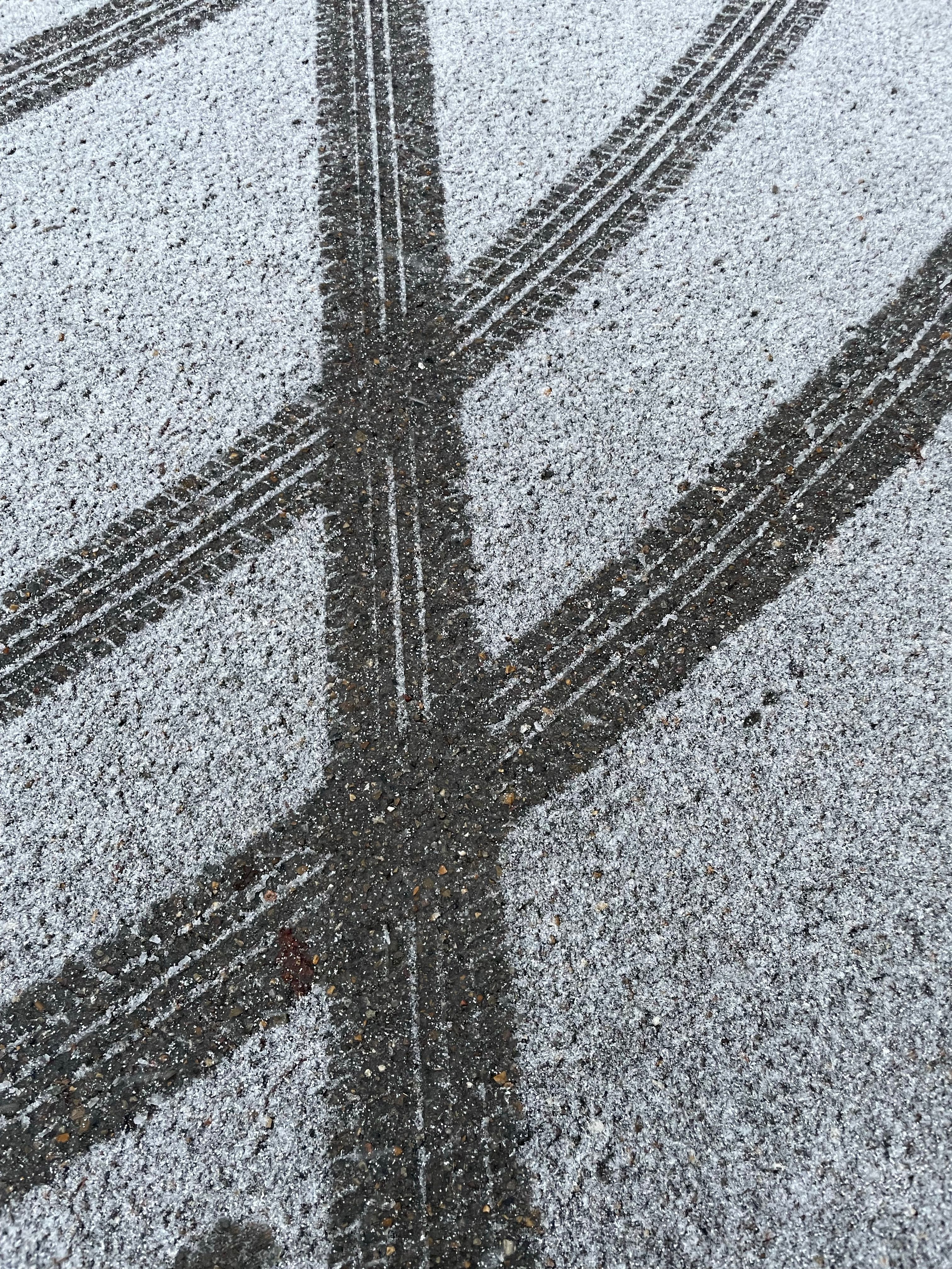 Close-up of crossing tire tracks on a snowy asphalt surface revealing winter conditions.