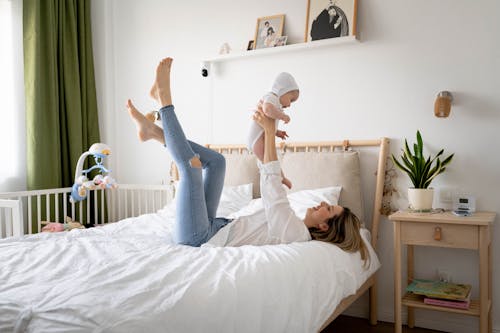 Free Mother Lying on the Bed and Holding Her Baby in the Air Stock Photo