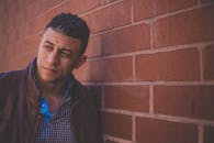 一位穿着皮夹克的自信男模特靠在砖墙上