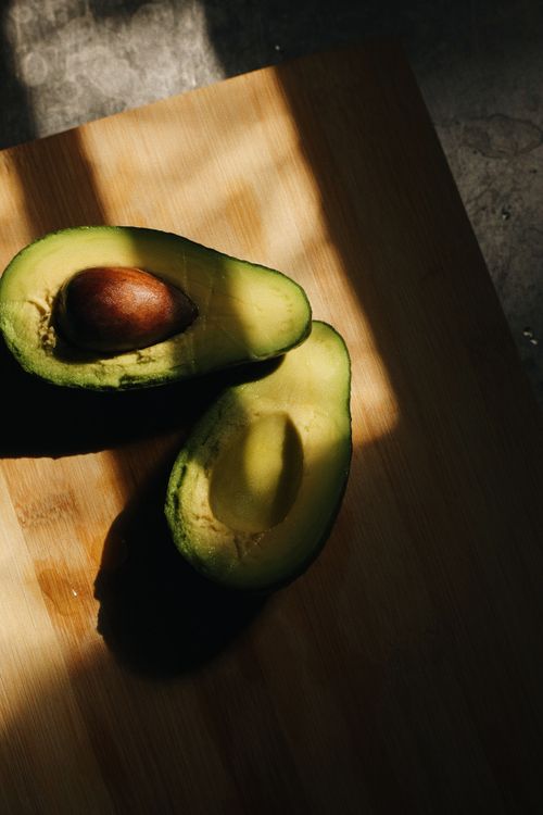 Free A cut avocado on a wooden board in natural sunlight, casting shadows for a dramatic effect. Stock Photo