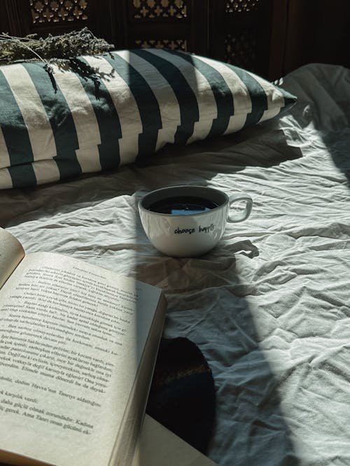 Open Book and Cup on Cozy Bed Sheets