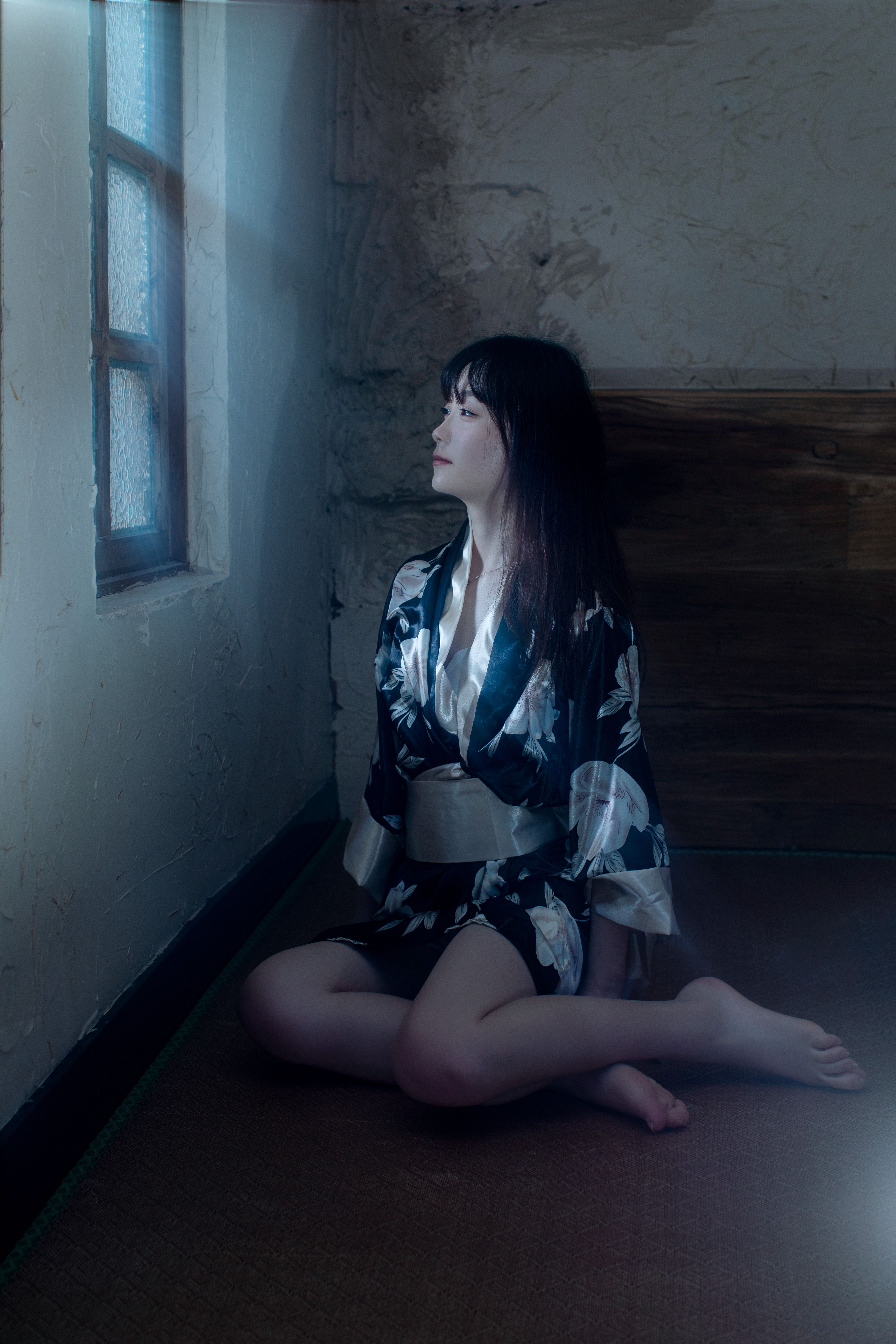 Woman in traditional attire meditating by a window, serene and thoughtful atmosphere.
