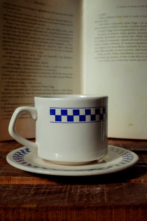 A cup and saucer on a table next to an open book
