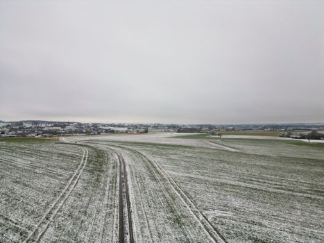 A serene rural landscape with light snow cover under a cloudy winter sky.