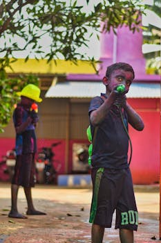 Two boys covered in vibrant colors enjoying water play outdoors during Holi festival.