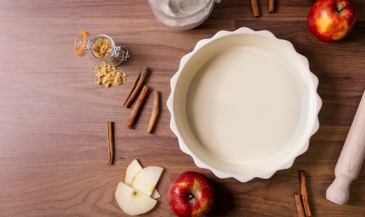 Empty cream white fluted pie dish with apples and cinnamon sticks