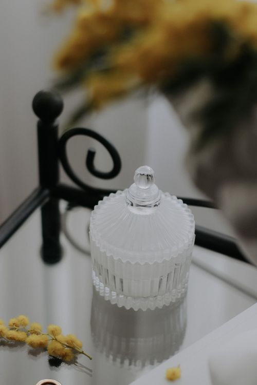 Free A decorative glass jar on mirrored table with soft lighting and floral accents. Stock Photo