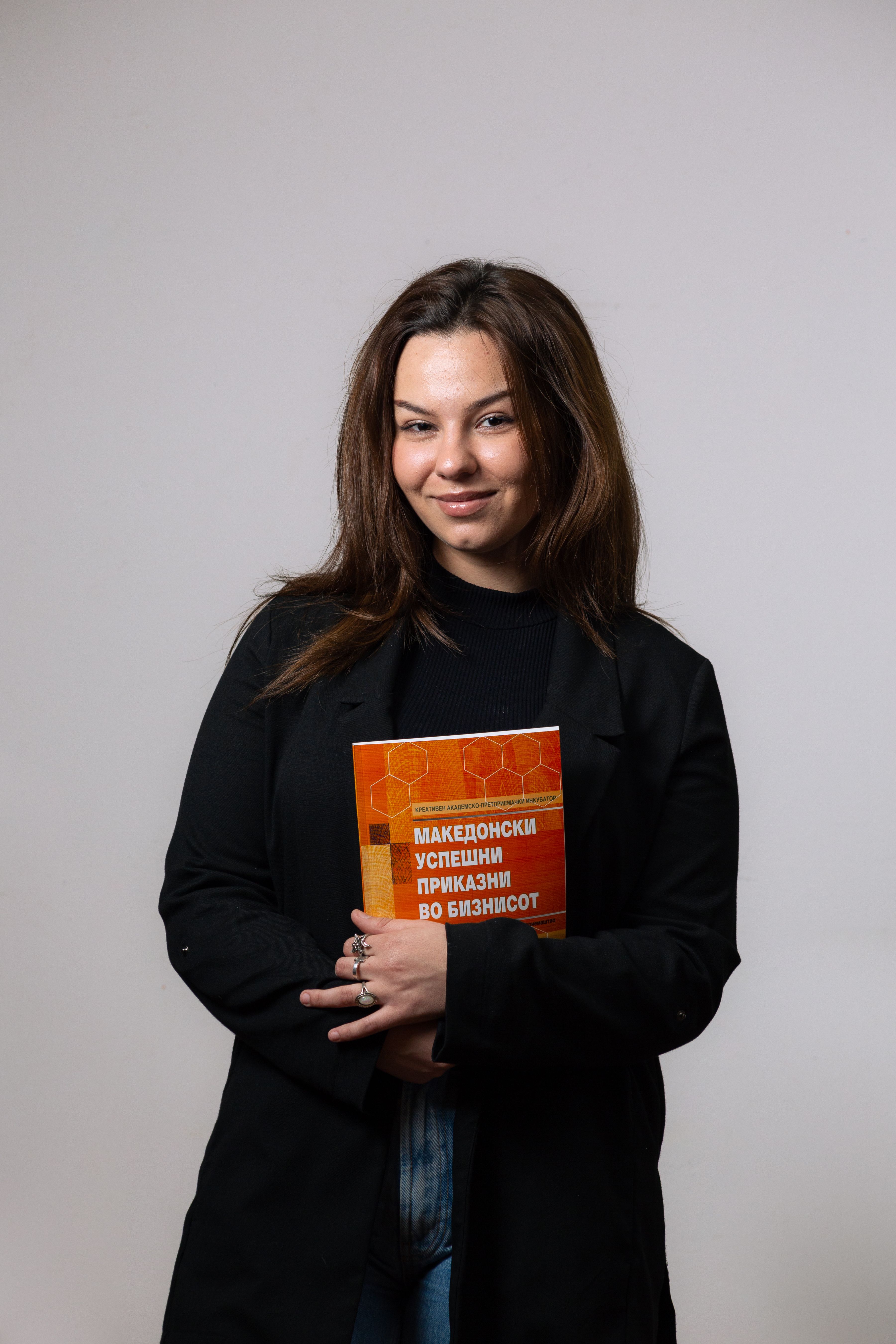 Young woman holding a Macedonian book and smiling confidently in a studio setting.