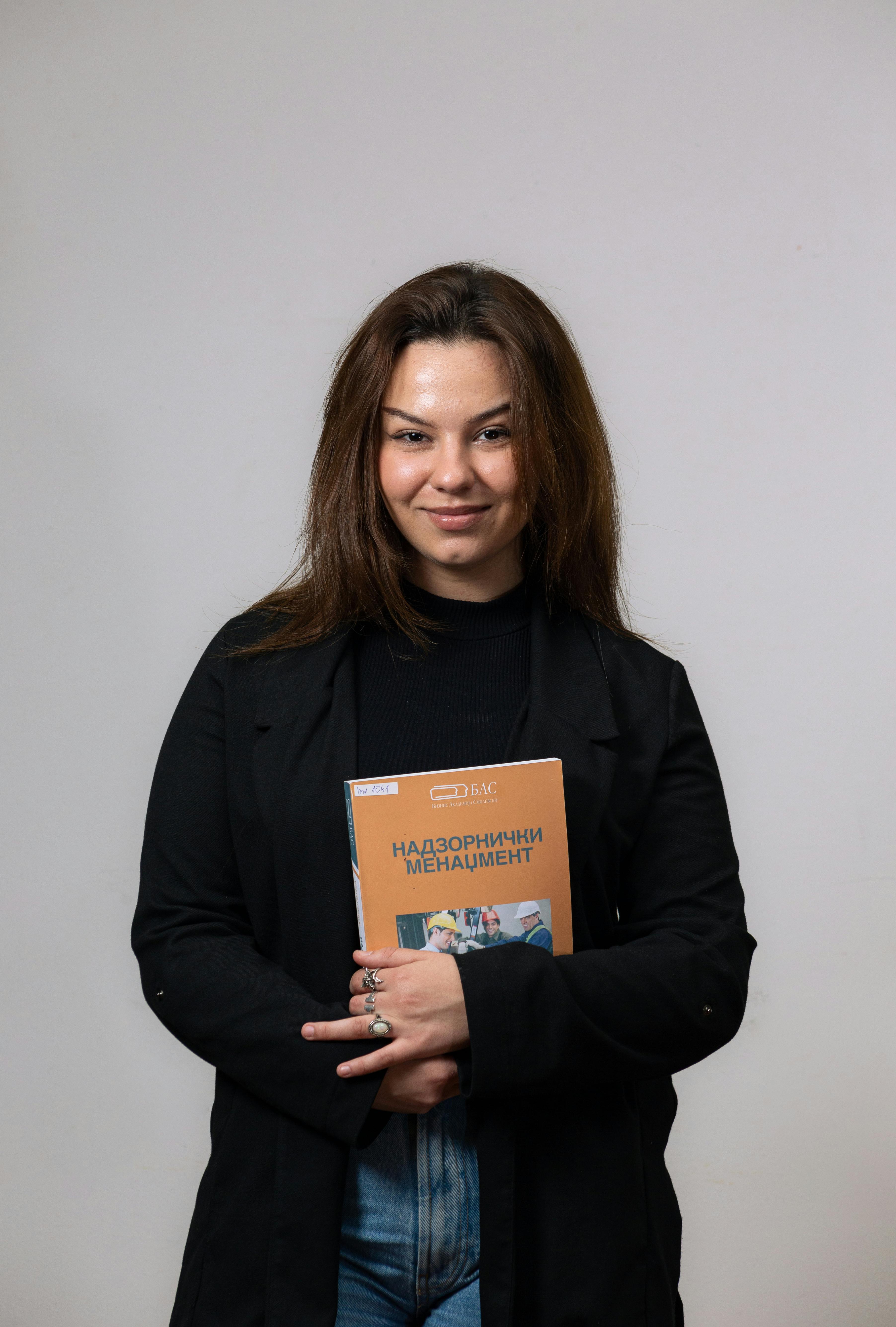 Portrait of a smiling young woman holding a textbook, showcasing education and learning.