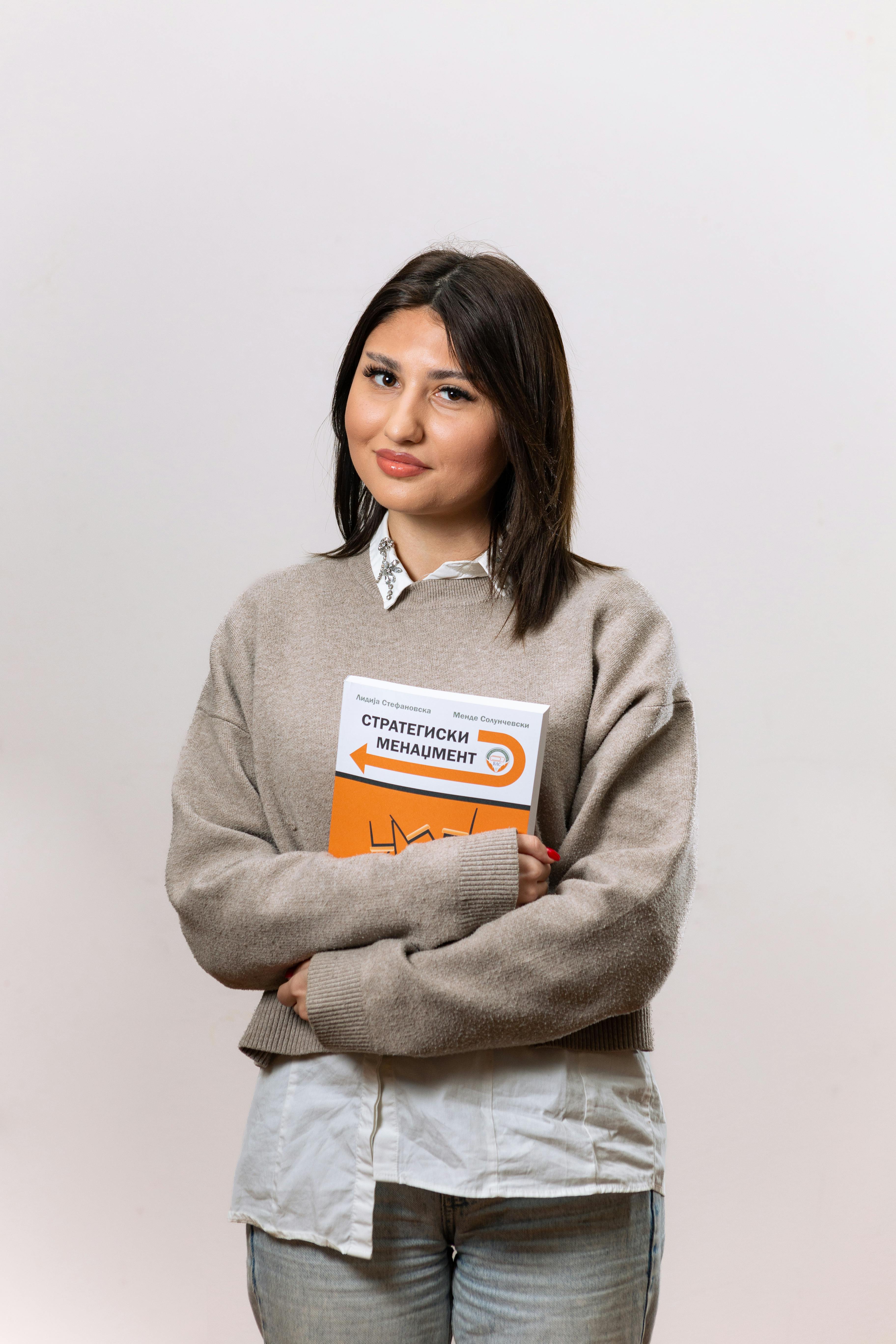 Confident woman holding a strategic management book in a studio setting, showcasing professional style.