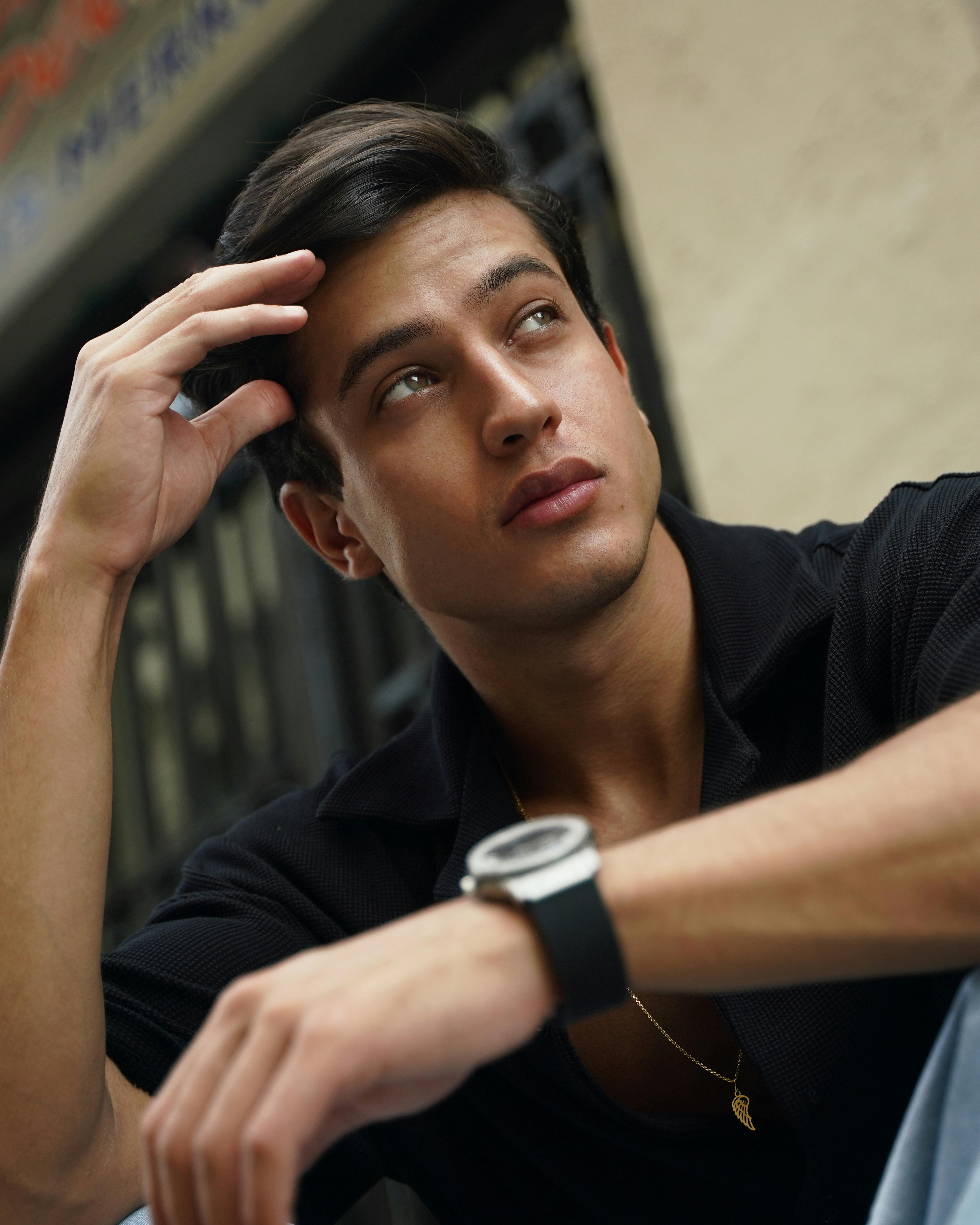 Free Captivating portrait of a young man sitting thoughtfully in an outdoor urban environment. Stock Photo