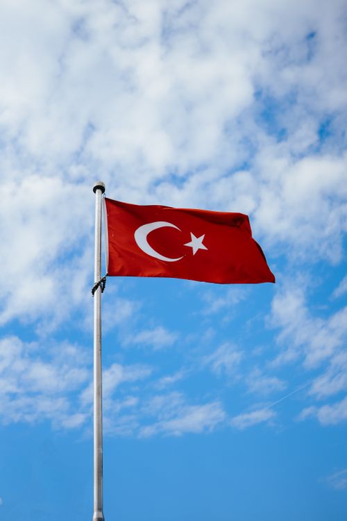 Free Red Turkish flag with crescent and star waving against a bright blue sky with clouds. Stock Photo