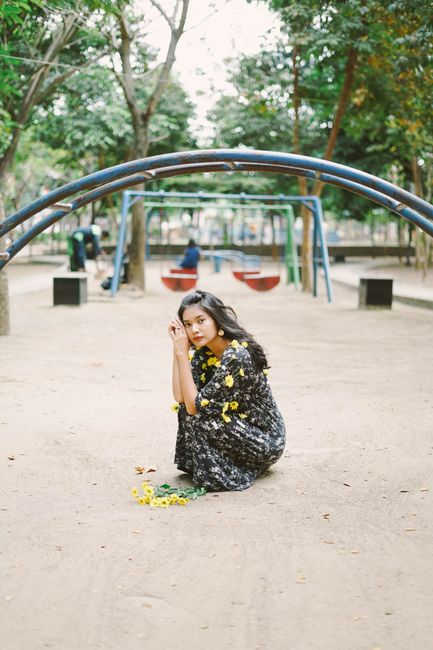 Young woman in floral dress with yellow flowers, sitting in a playground, exuding calmness.