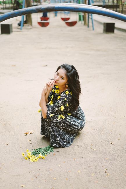 A young woman kneels in a floral dress with yellow flowers at a playground.