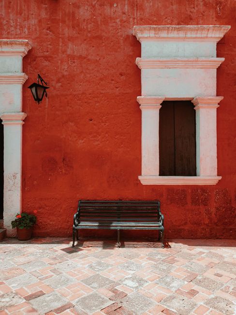 A serene corner in a charming city with a bench against a vibrant red wall, perfect for relaxation.